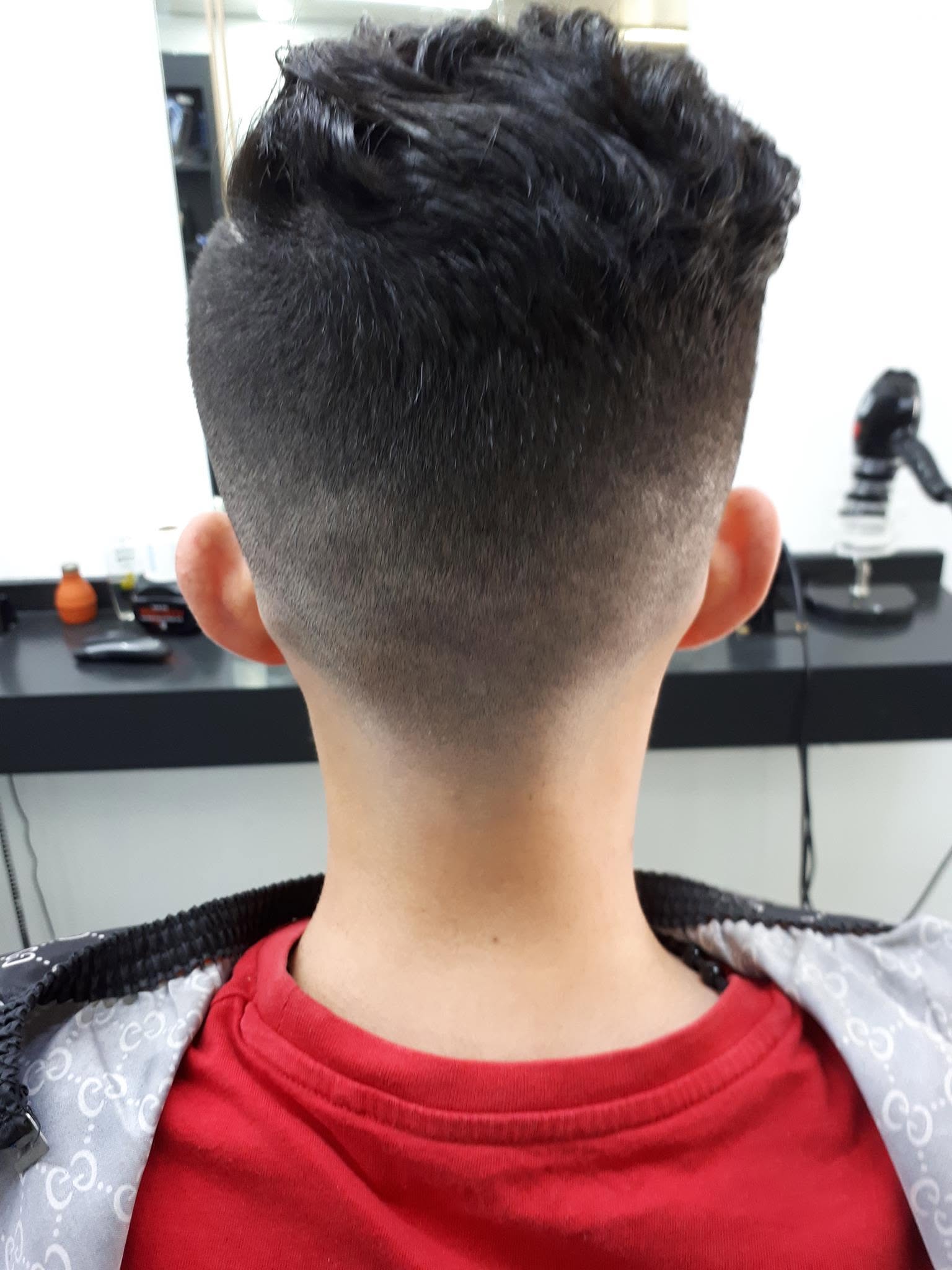 Achterhoofd van een klant in een rood shirt: een strakke fade die kort in de nek begint