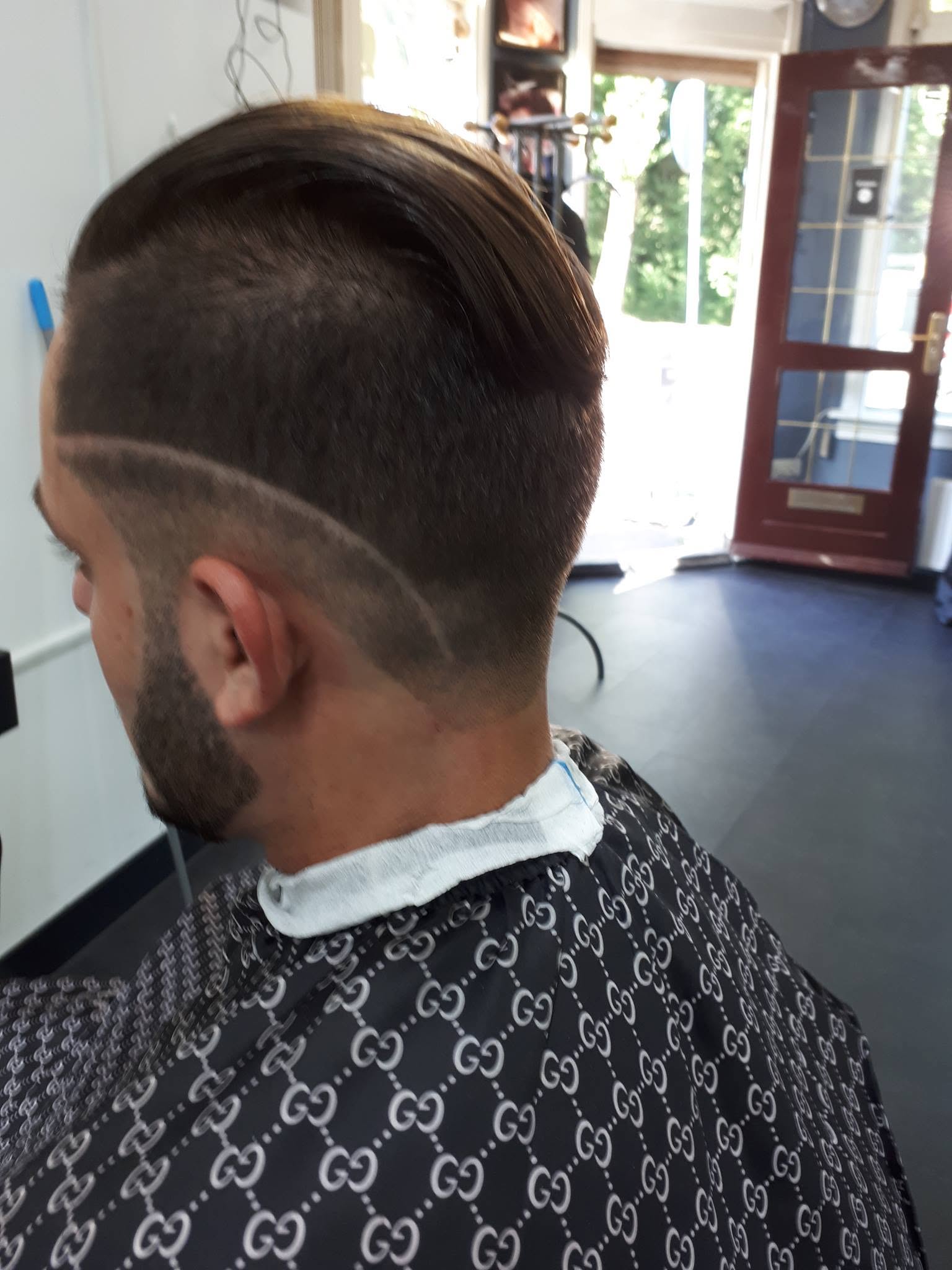 Klant van opzij gezien: korte fade met een geschoren lijn, de deur van de zaak op de achtergrond