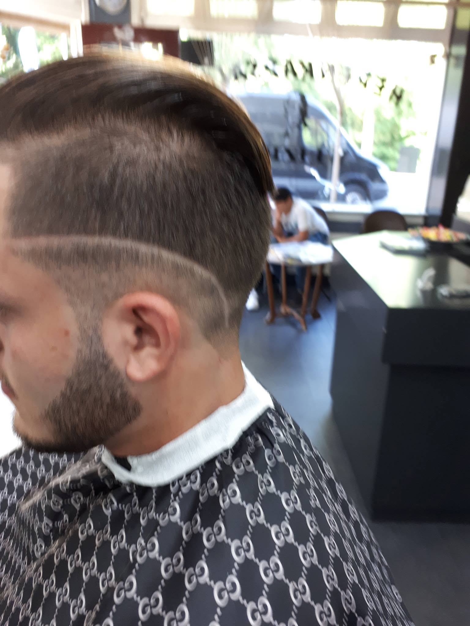 Klant met baard en een fade met geschoren lijn, de etalage van de zaak op de achtergrond